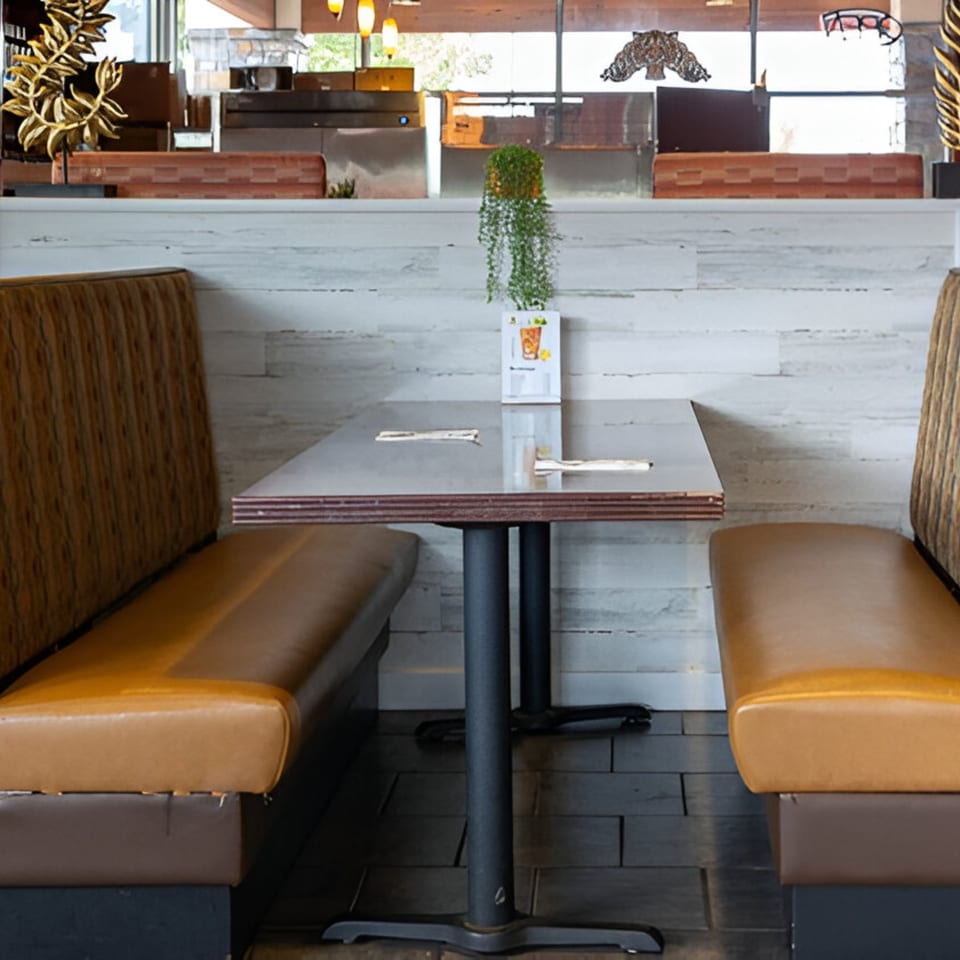 Empty booth seating with a dark table and light wood paneling at Wild Tiger Thai restaurant.