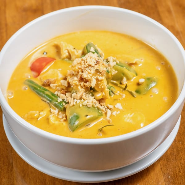 Wild Tiger Thai yellow curry with chicken, green beans, avocado, and crushed peanuts in a white bowl.