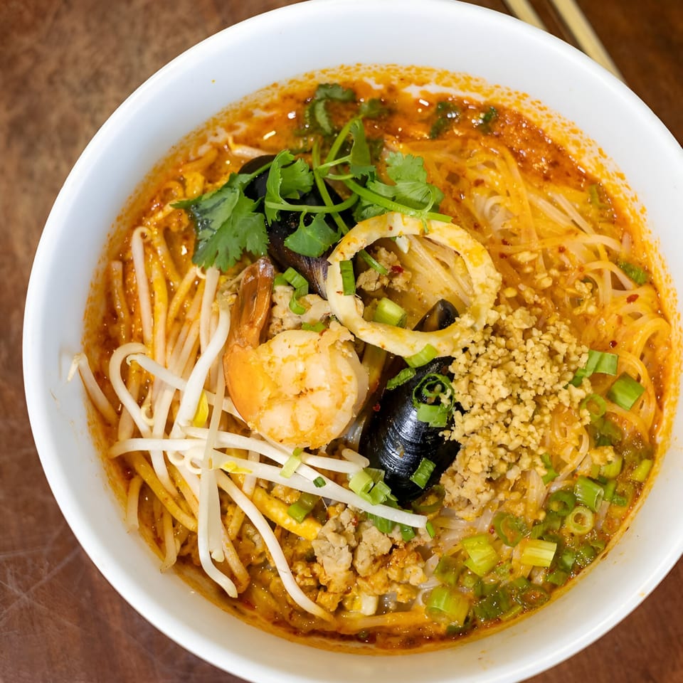 Close-up of a vibrant Thai noodle soup with shrimp, mussels, squid, cilantro, and bean sprouts.