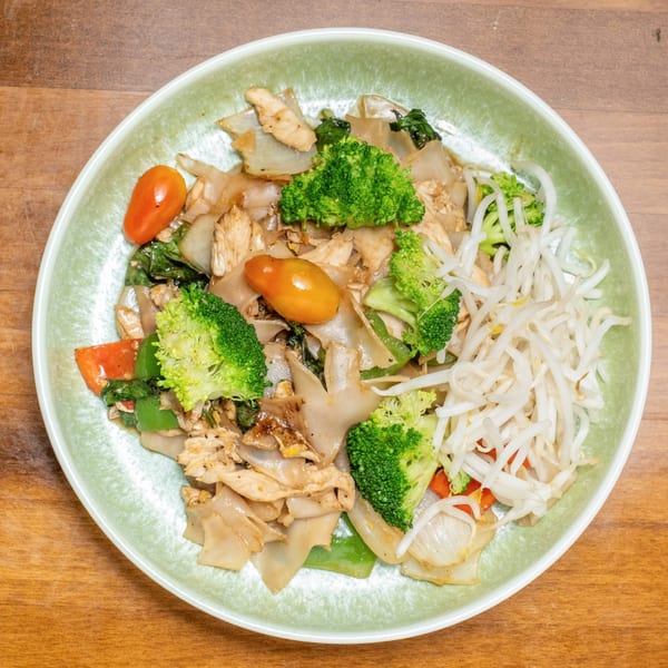Wild Tiger Thai's Pad See Ew with chicken, broccoli, tomatoes, and bean sprouts in a light green bowl.