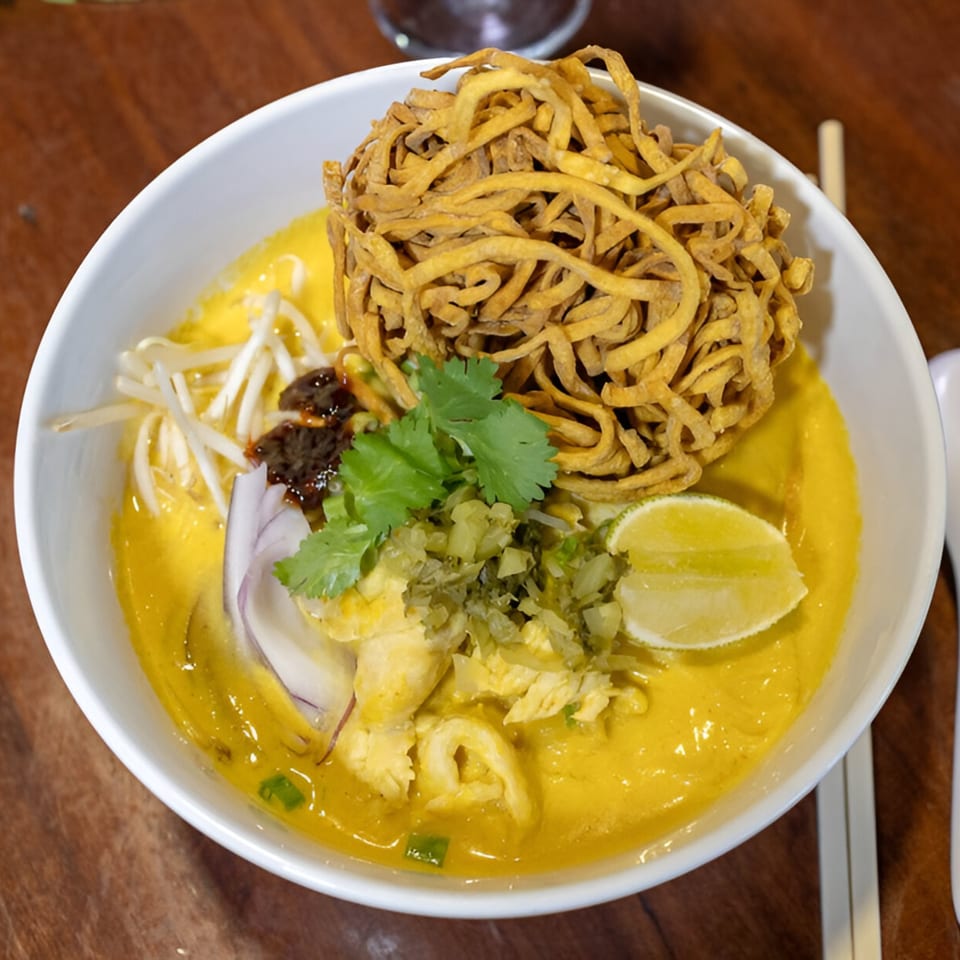 A bowl of Wild Tiger Thai Khao Soi with crispy noodles, lime, cilantro, and bean sprouts.