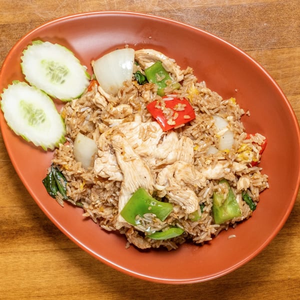 Wild Tiger Thai chicken fried rice with bell peppers, onions, and cucumber slices on a red plate.