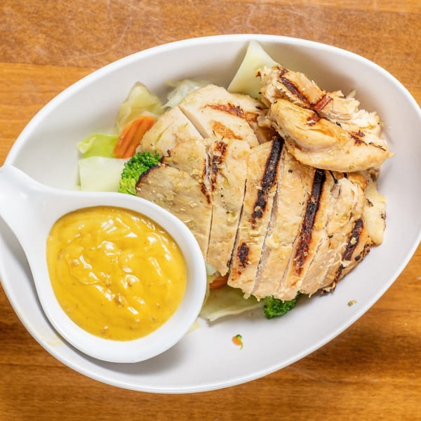 Grilled chicken slices with vegetables and a side of yellow curry sauce in a white bowl.