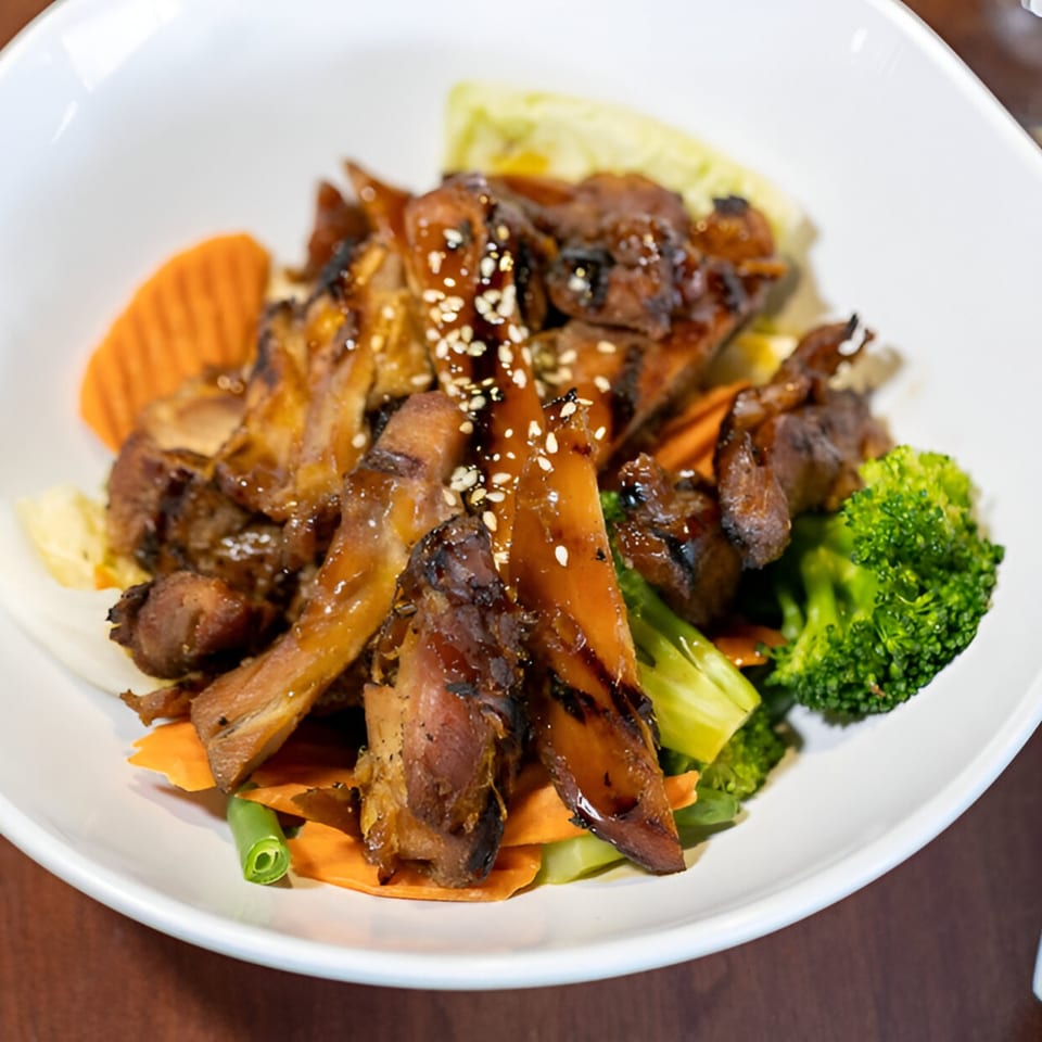 Wild Tiger Thai's grilled chicken with sesame seeds, broccoli, and carrots in a white bowl.